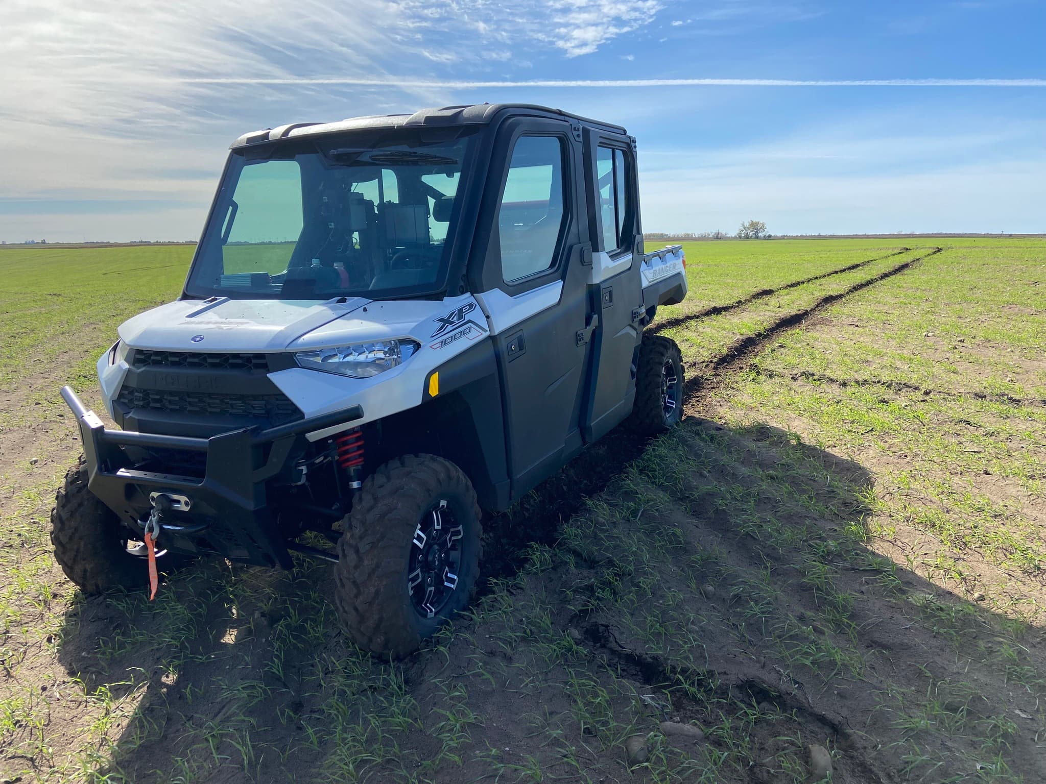 White Polaris Ranger XP 1000 UTV parked in a green field with visible tire tracks.